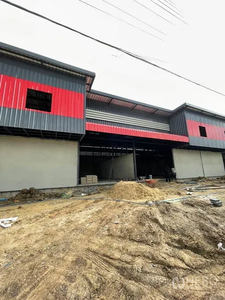 Warehouse for rent in Pathum Thani - Row of connected warehouse units with red accents and unfinished frontage.