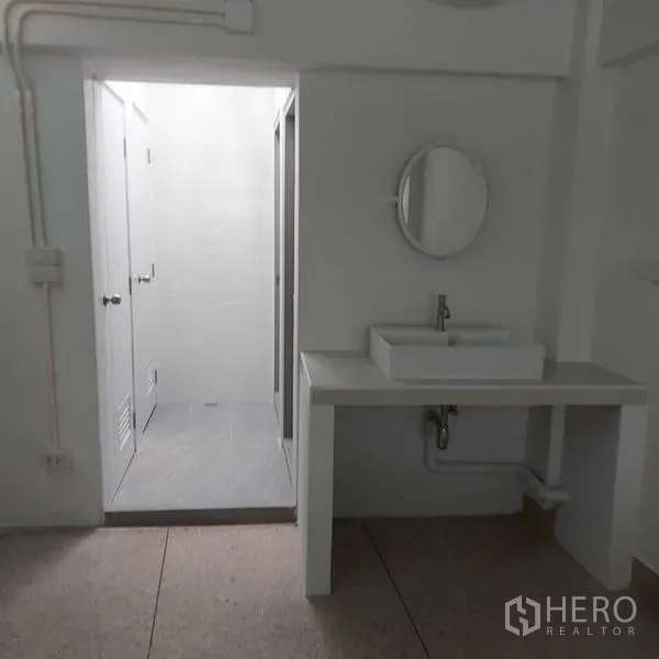 Shophouse for rent in Khlong Toei, Bangkok - Clean restroom with vanity sink, round mirror and separate toilet–shower area.