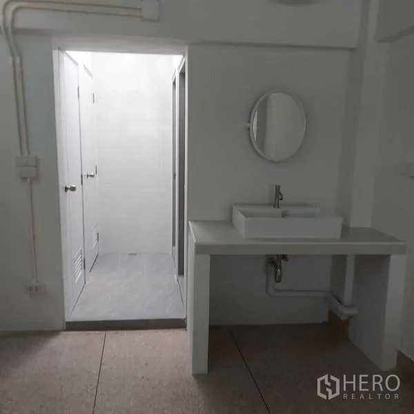 Shophouse for rent in Khlong Toei, Bangkok - Clean restroom with vanity sink, round mirror and separate toilet–shower area.