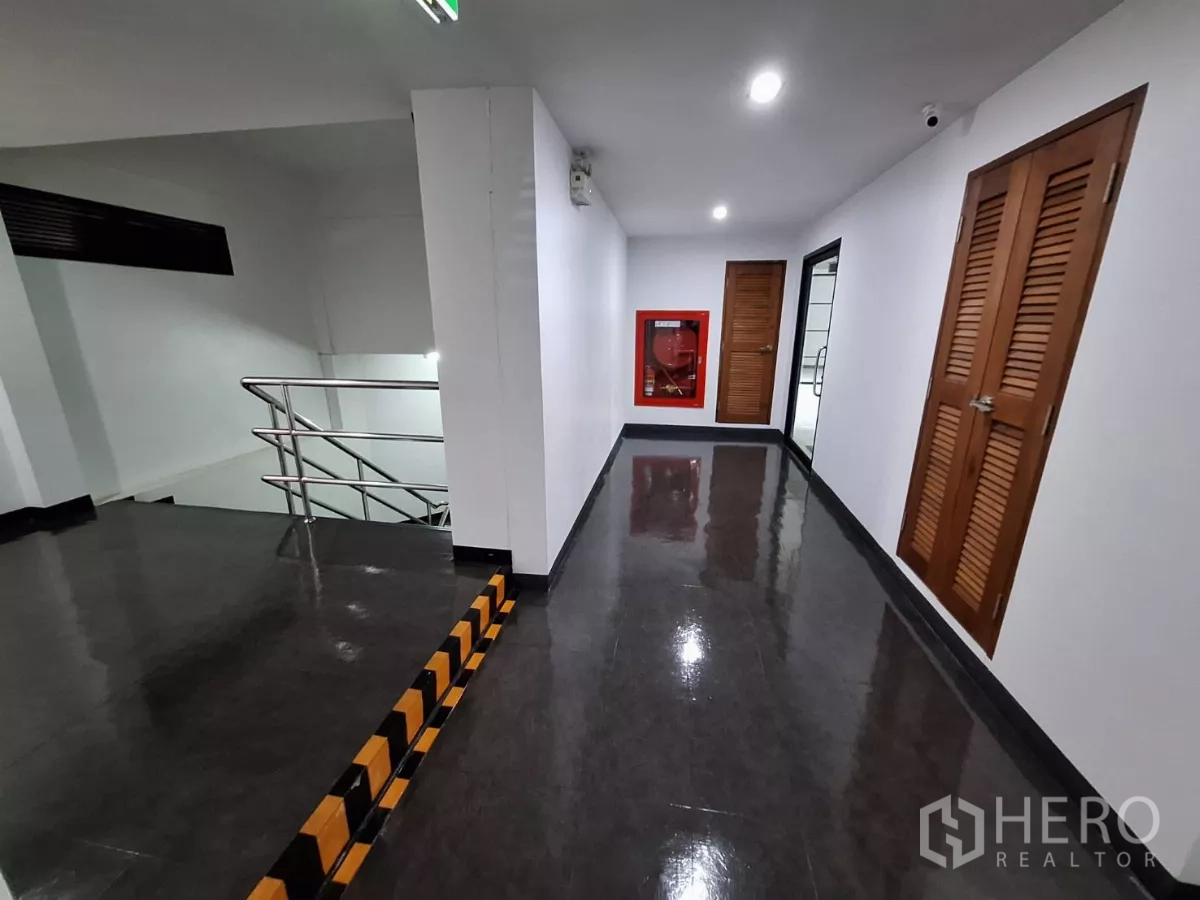 Office Space for rent in Watthana, Bangkok - Building corridor with stainless handrail, glossy floors, and illuminated exit sign.