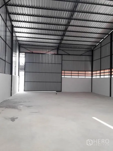 货栈 出租在Lam Luk Ka, Pathum Thani - 开阔存储区，面向大型金属卷闸门与带通风的墙板。