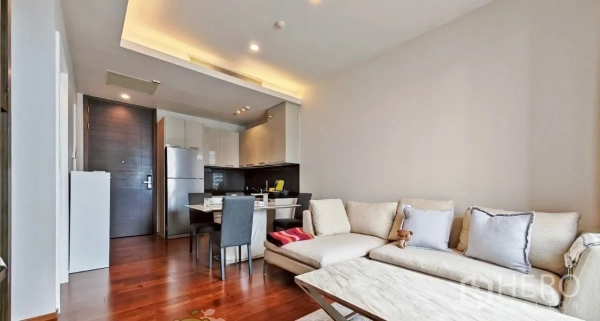 Condominium for rent in Watthana, Bangkok - Open-plan lounge with sofa, dining table, and compact kitchen, highlighted by warm recessed lighting and wood floors.