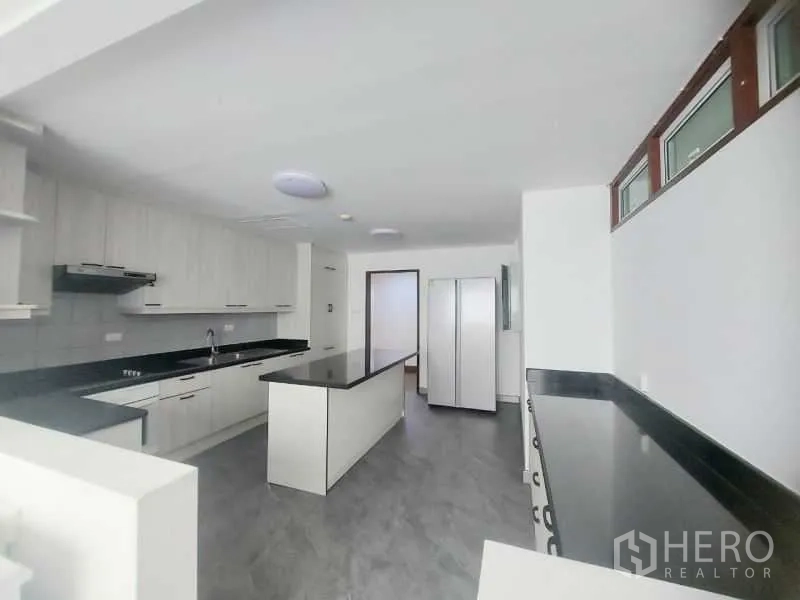 Condominium for rent in Watthana, Bangkok - Kitchen from another angle showing long counters, cooktop, range hood and tall fridge space.