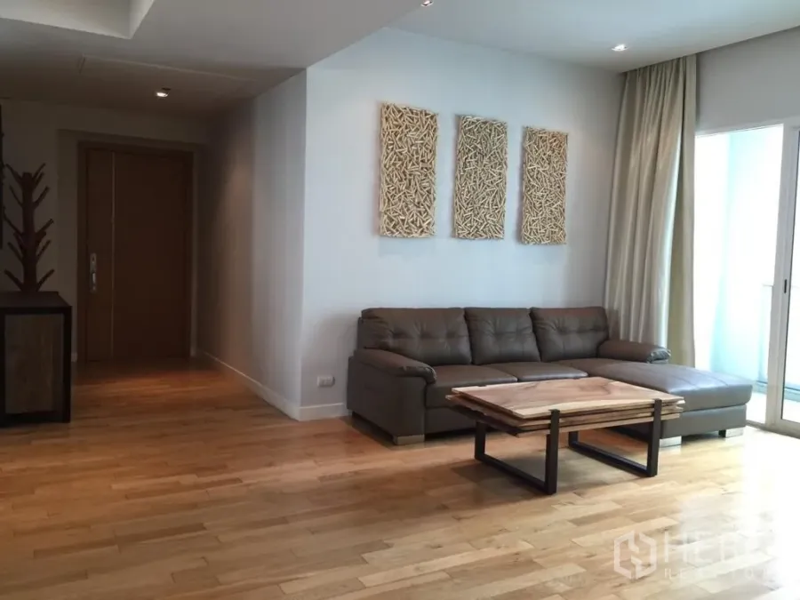 Condominium for rent or sale in Khlong Toei, Bangkok - Bright living room with L-shaped leather sofa, wood floors and balcony access in a Khlong Toei condo.