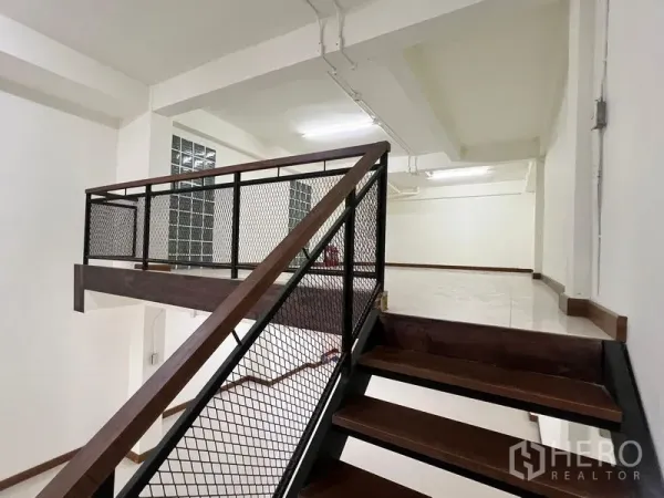 Shophouse for rent in Khlong Toei, Bangkok - Steel-and-wood staircase with mesh railing leading up to a mezzanine level.