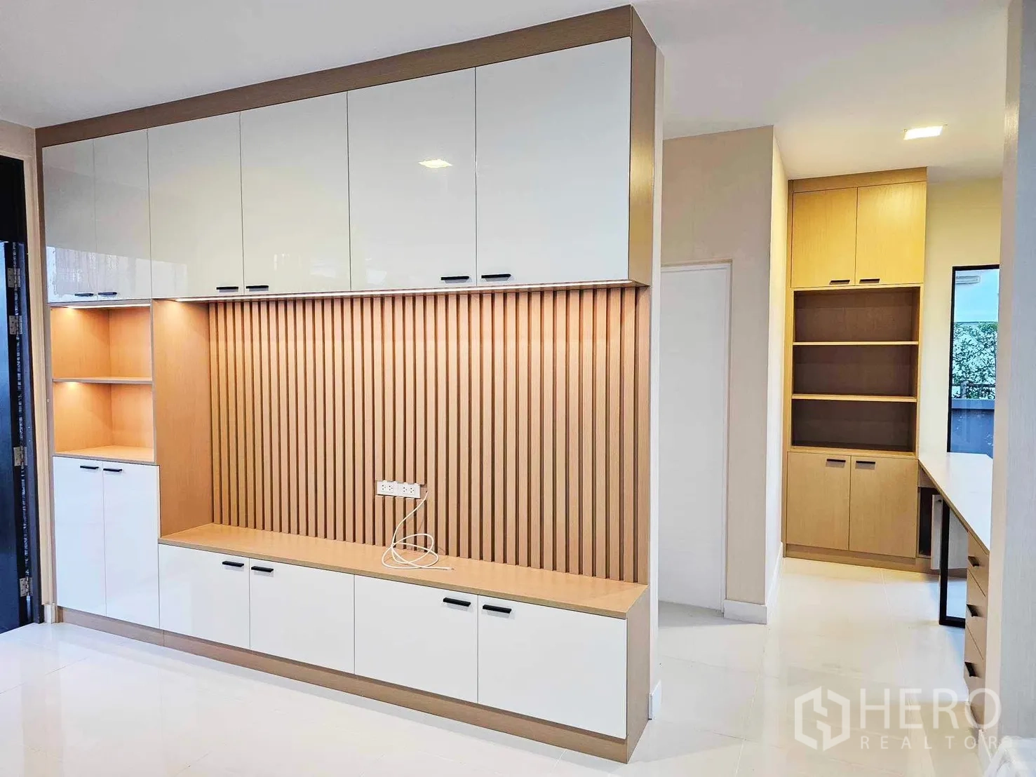 Detached House for rent or sale in Prawet, Bangkok - Built-in TV wall with white and wood cabinetry, accent lighting and adjoining storage shelves.
