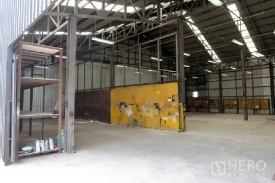 Warehouse for rent in Pak Kret, Nonthaburi - Entry view of the warehouse with a metal shelving unit and yellow divider wall.