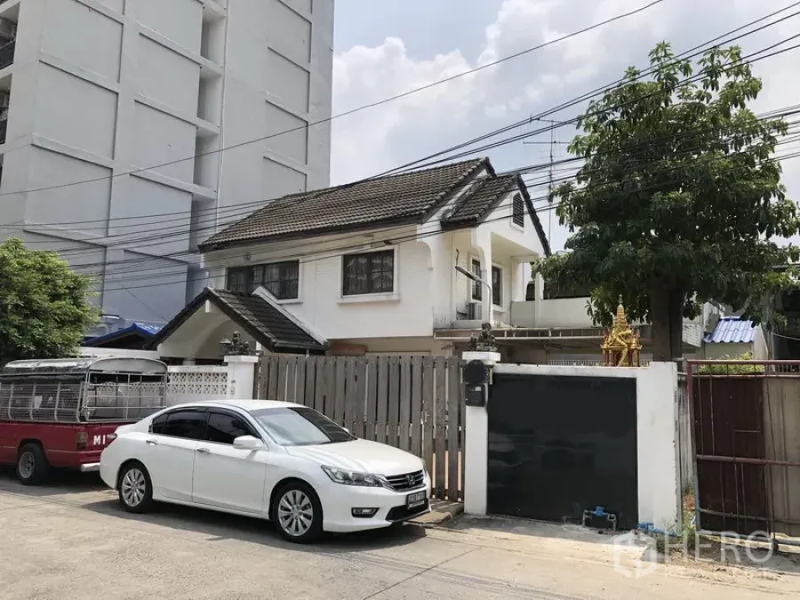 Detached House for sale in Pak Kret, Nonthaburi - Front street view of a two‑storey white detached house with wooden gate, driveway and parked cars.