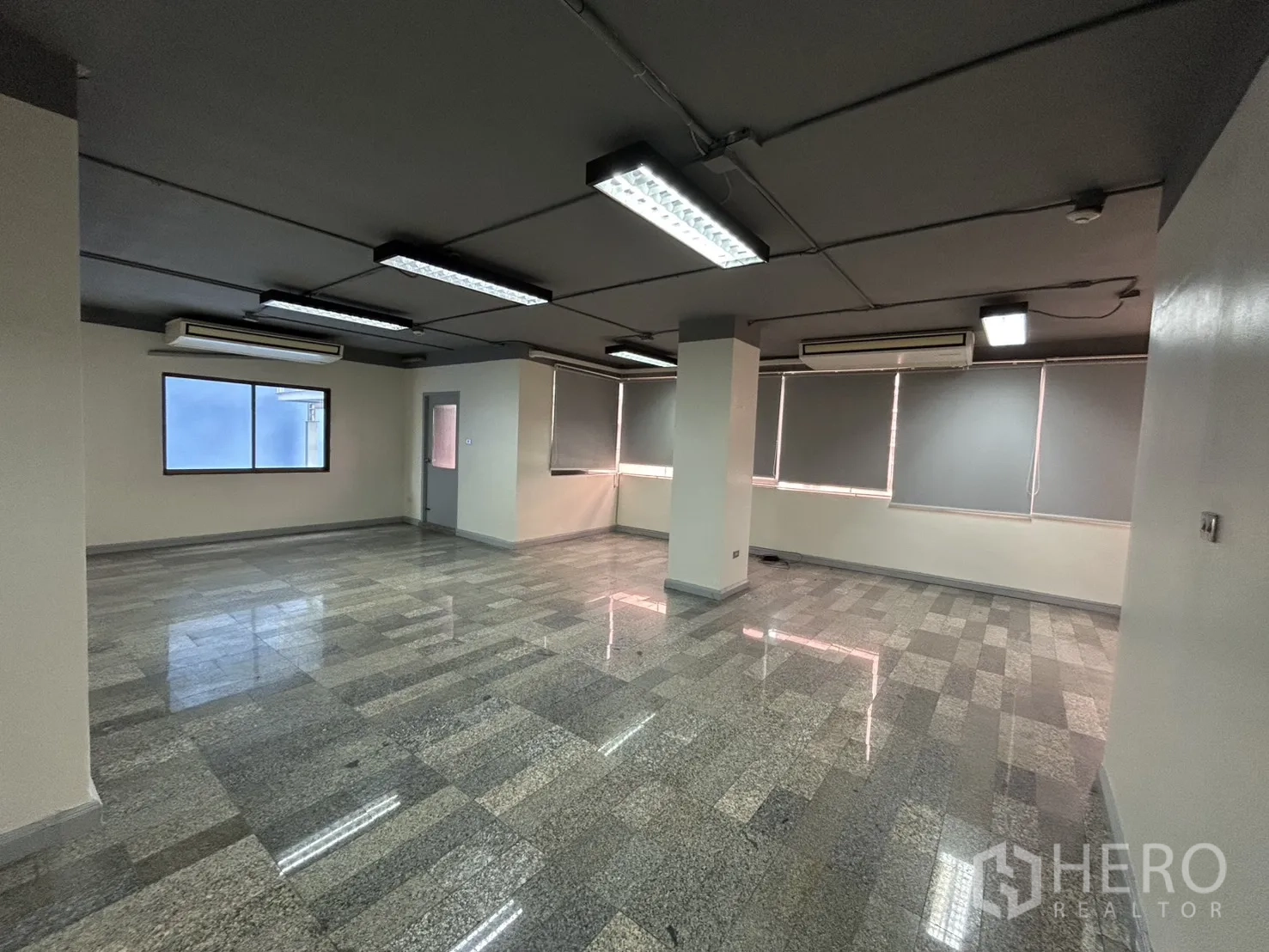 Office Space for rent in Khlong Toei, Bangkok - Spacious office area showing windows, air-conditioning units, multiple light fixtures, and gray tile flooring.
