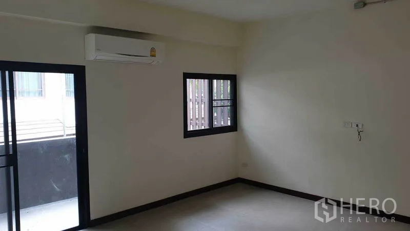 Townhouse for rent or sale in Khlong Toei, Bangkok - Bedroom corner with balcony access and window, fitted with air conditioner.