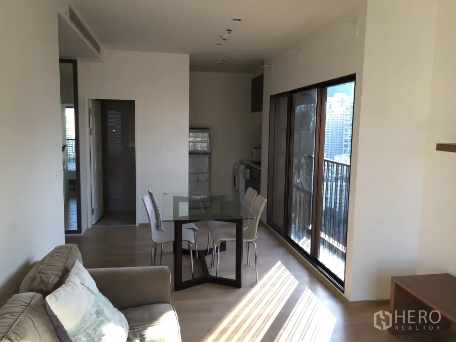 Condominium for rent in Bangkok - Open-plan lounge with dining set, compact kitchenette with washer and sliding doors to a balcony overlooking Bangkok skyline.