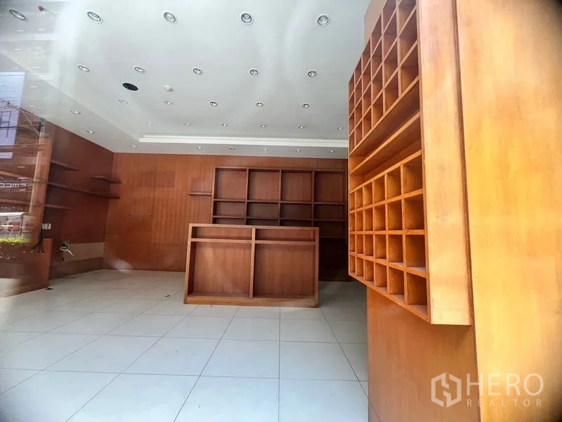 Retail Space for rent in Khlong Toei, Bangkok - Shop interior with built-in wooden shelving, central display counter, and white tiled floor under spotlights.