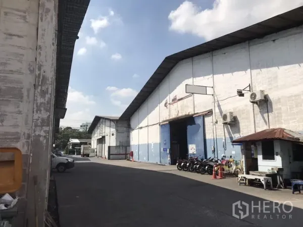 Warehouse for rent in Khlong Toei, Bangkok - Warehouse facade with a high roller door, covered driveway, parked motorcycles, and a small guard booth.