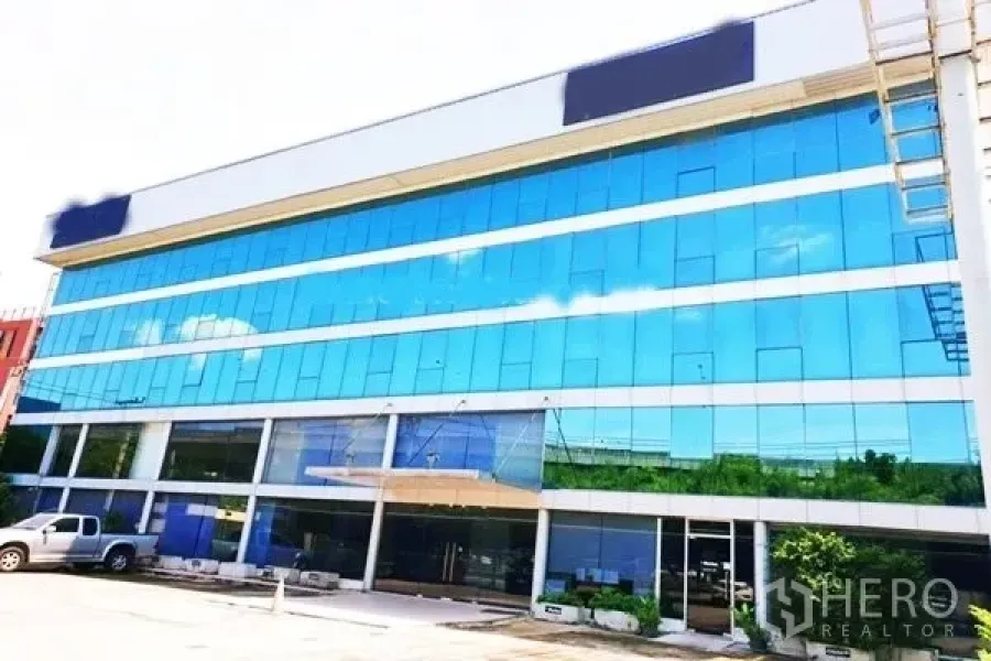 Office Space for rent in Suan Luang, Bangkok - Modern mid-rise office building with reflective blue glass façade and surface parking.