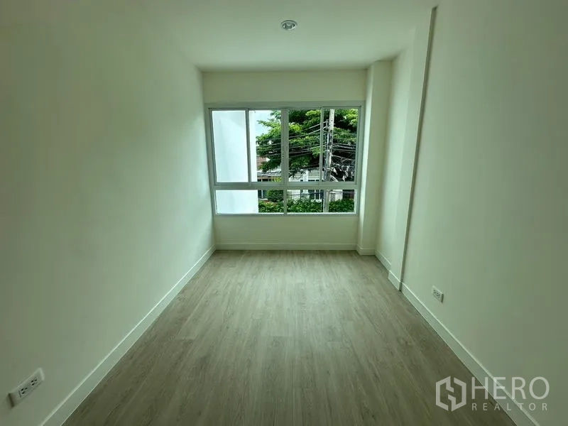 Home Office for rent in Khlong Toei, Bangkok - Narrow bedroom with green view through a wide window and pale wood floor.