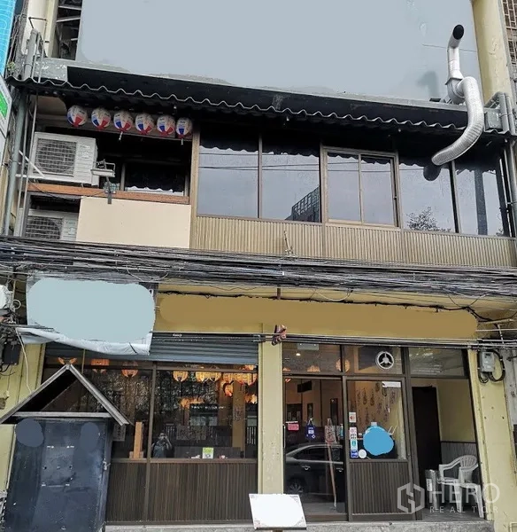 Shophouse for rent in Watthana, Bangkok - Street-facing shophouse facade in Watthana with wide glass storefront, upper-floor windows and exterior kitchen exhaust, ideal for a restaurant.