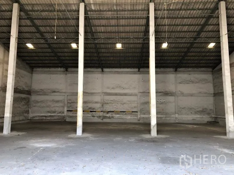 Warehouse for rent in Lat Krabang, Bangkok - Spacious warehouse interior with high ceiling, steel trusses, concrete floor and central support columns illuminated by overhead lights.