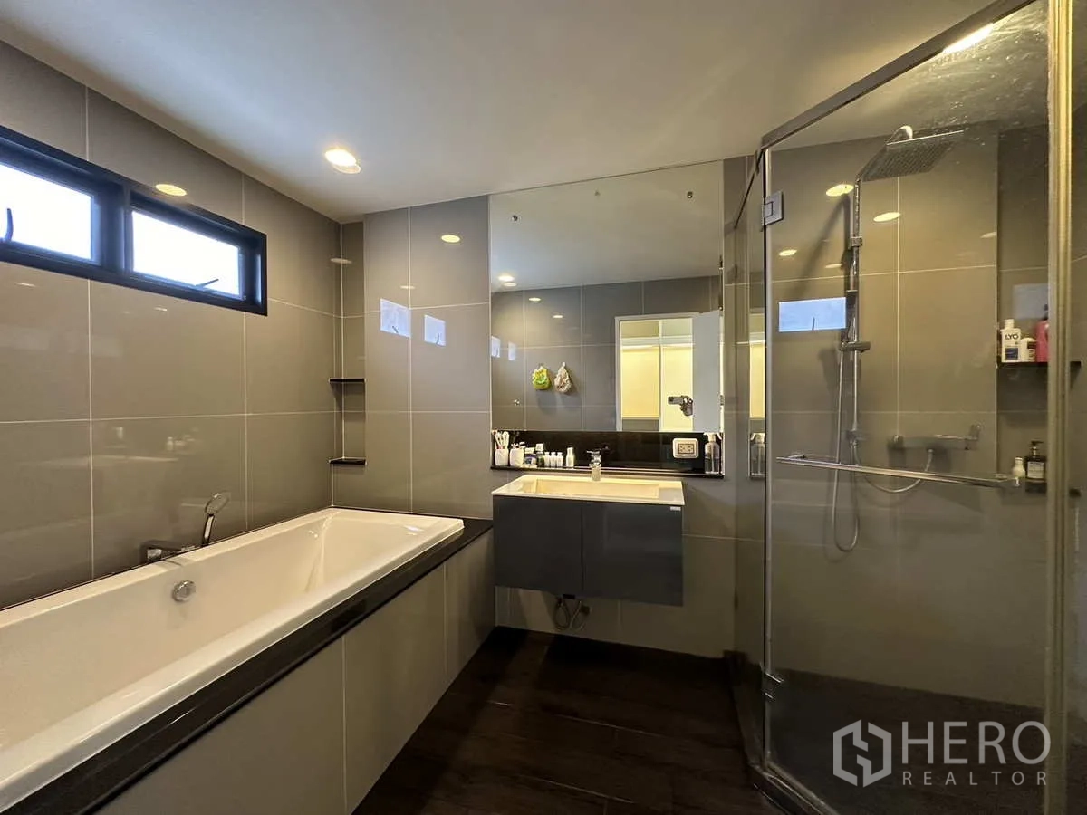 Detached House for rent or sale in Lam Luk Ka, Pathum Thani - Modern bathroom with bathtub, glass shower and large mirror.