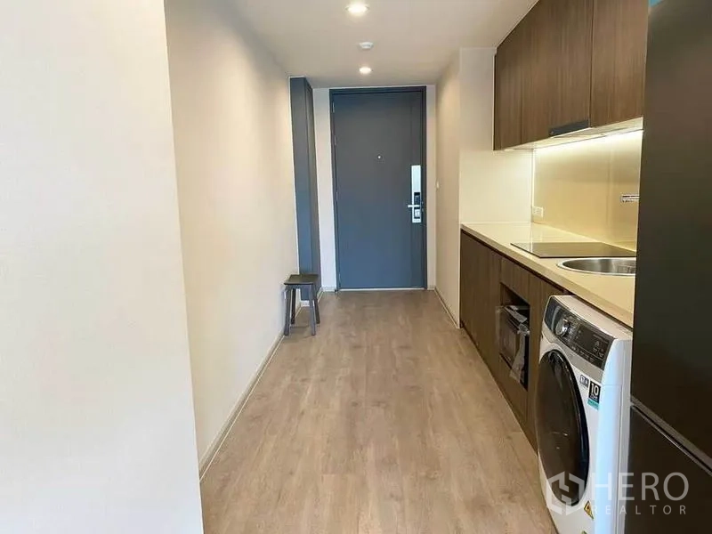 Condominium for rent in Pathum Wan, Bangkok - Galley kitchen corridor with built-in cabinets, cooktop, sink, oven, refrigerator and washing machine.