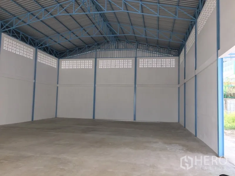 工厂 出租在Pathum Thani - 高挑宽敞的厂房内部，蓝色钢结构屋架与通风砖窗，混凝土地坪。