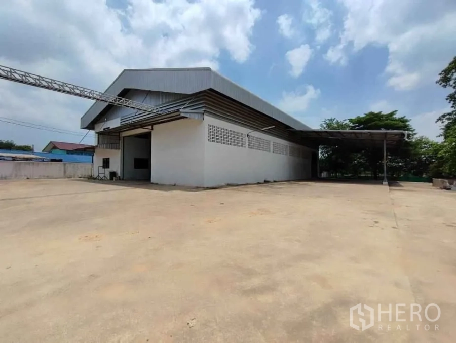 Factory for rent in Mueang Chachoengsao, Chachoengsao - Factory building with large concrete yard and covered loading area under blue sky.