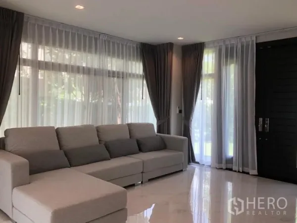 Detached House for rent in Bang Phli, Samut Prakan - Airy living room featuring a large L-shaped sofa, sheer curtains and full-height windows.