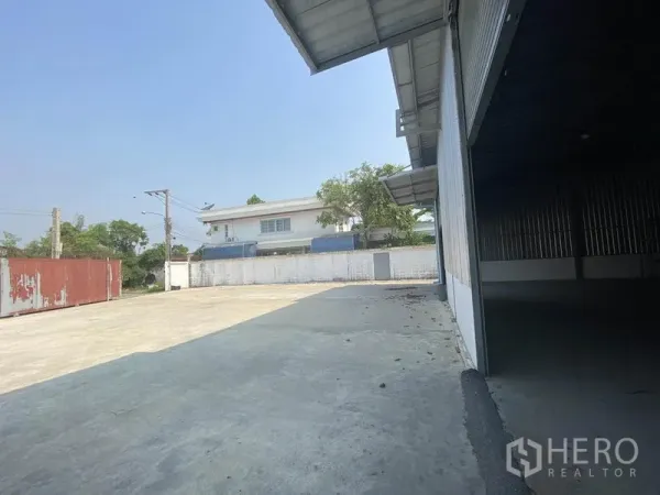 Warehouse for rent in Prawet, Bangkok - Side view of loading area showing large paved driveway, boundary wall, and access gate.