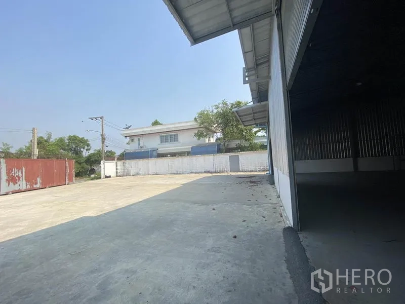 Warehouse for rent in Prawet, Bangkok - Side view of loading area showing large paved driveway, boundary wall, and access gate.