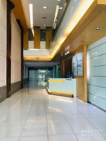 Office Space for rent in Ratchathewi, Bangkok - Double-height lobby with reception desk, glossy white tiles, and warm ceiling lights in a modern office building.