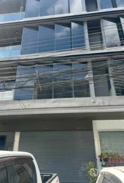 Retail Space for rent in Khlong Toei, Bangkok - Modern low-rise building exterior with reflective glass facade, balcony rails, roller shutter and parked cars.