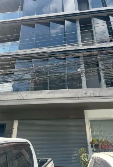 Retail Space for rent in Khlong Toei, Bangkok - Modern low-rise building exterior with reflective glass facade, balcony rails, roller shutter and parked cars.