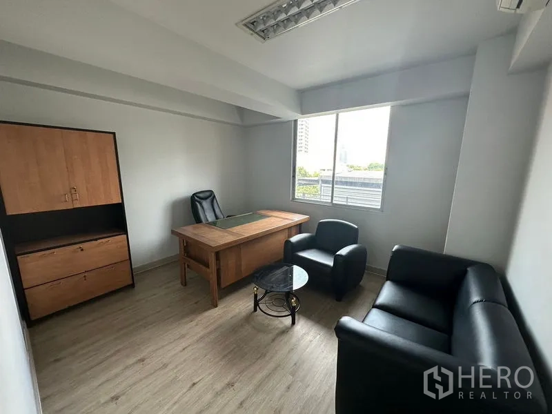 Office Space for rent in Khlong Toei, Bangkok - Private executive room featuring a wooden desk, black leather sofa set, window with natural light, and a matching storage cabinet.