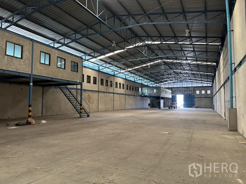 Warehouse for rent in Bang Phli, Samut Prakan - Clear-span warehouse floor with 9 m ceiling, steel beams, and dual staircases to mezzanine offices.