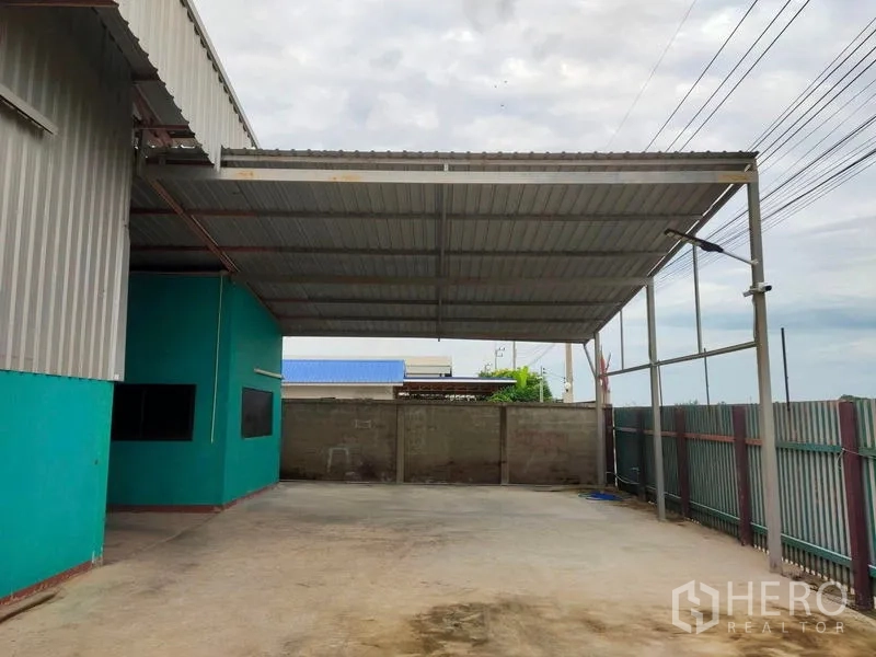 Warehouse for sale in Lam Luk Ka, Pathum Thani - Covered loading bay with high steel canopy and fenced hardstand for trucks.