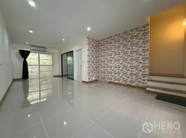 Townhouse for rent in Suan Luang, Bangkok - Spacious open-plan living room with feature brick wall and stairway.