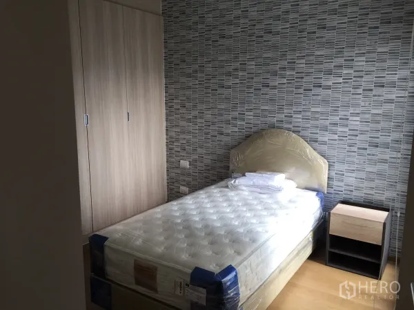 Condominium for rent in Pathum Wan, Bangkok - Cozy bedroom with single bed, built-in wardrobe and textured feature wall.