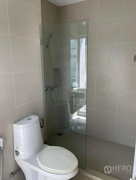 Townhouse for rent in Suan Luang, Bangkok - Modern bathroom with beige tiles, glass-enclosed shower and white toilet.