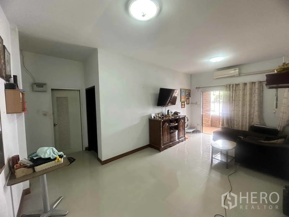 Detached House for sale in Pathum Thani - Bright living room with tiled floors, wall-mounted TV, and sliding door to the terrace.