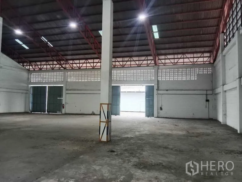 Factory for rent in Samut Prakan - Central aisle showing tall columns, lit roof panels, and ample floor space.