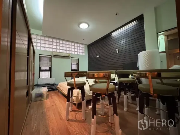 Shophouse for rent in Bang Rak, Bangkok - Multi-purpose room with wood flooring, glass-block clerestory windows, and stacked stools around a low bed.