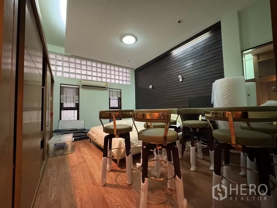 Shophouse for rent in Bang Rak, Bangkok - Multi-purpose room with wood flooring, glass-block clerestory windows, and stacked stools around a low bed.