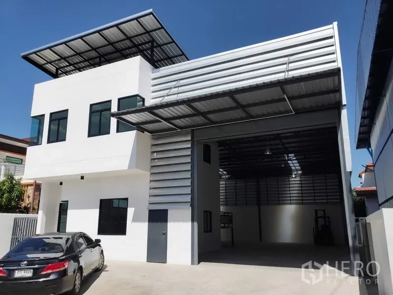 Factory for rent in Lam Luk Ka, Pathum Thani - Front of factory showing covered loading bay, metal cladding and wide parking driveway.