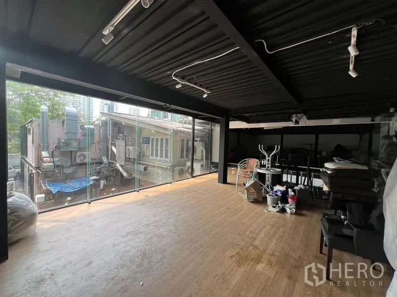 Retail Space for rent - Spacious retail floor with black exposed ceiling, track lighting, and a glass facade facing neighboring buildings.