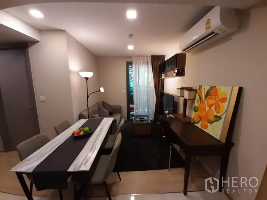 Condominium for rent or sale in Watthana, Bangkok - Open-plan living room with dining table, TV wall, work desk and balcony door in an Ekkamai condo.
