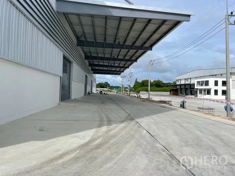 Factory for rent in Mueang Rayong, Rayong - Covered dock and side driveway beside power lines and neighboring industrial buildings.