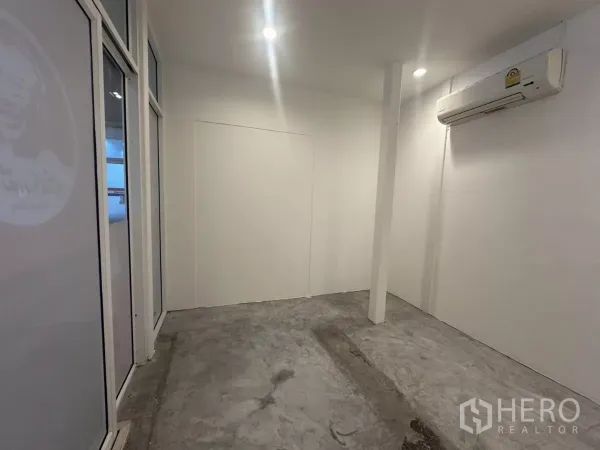 Retail Space for rent - Interior view toward the glass storefront with pillar, recessed lighting, concrete floor and wall-mounted AC unit.