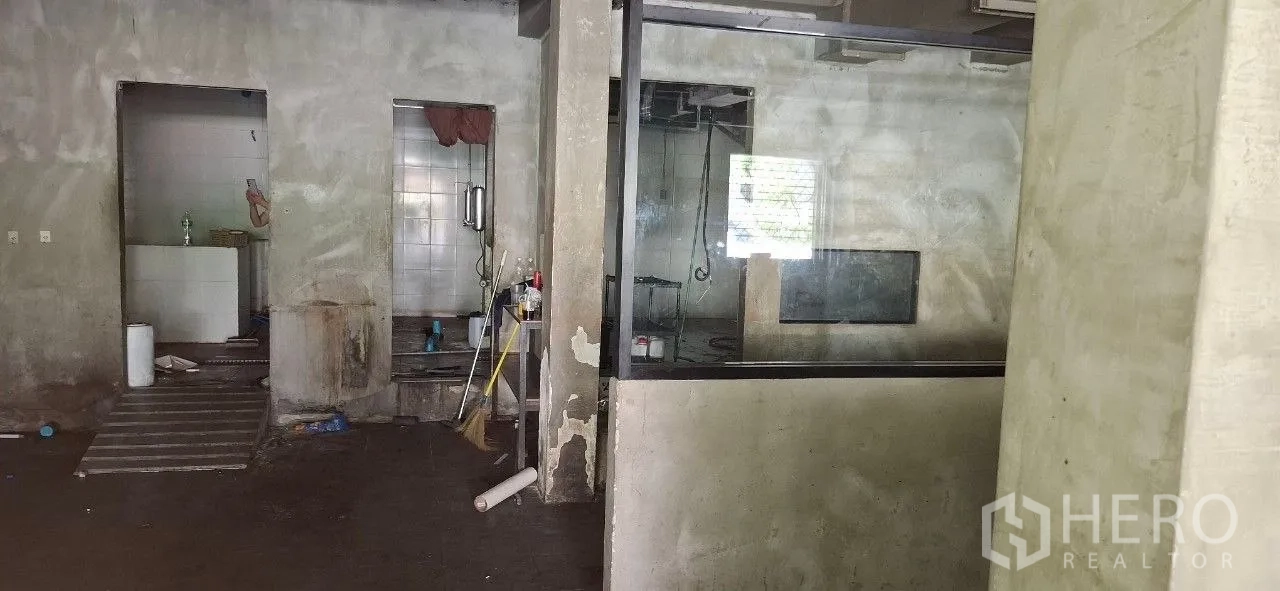 Shophouse for rent or sale in Watthana, Bangkok - Concrete room with glass partition and access to tiled back rooms in a retrofit-ready space.