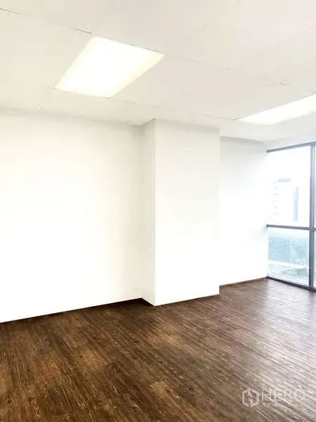 Office Space for rent - Bright corner workspace with wood floors, white walls and ceiling lights beside a tall window.