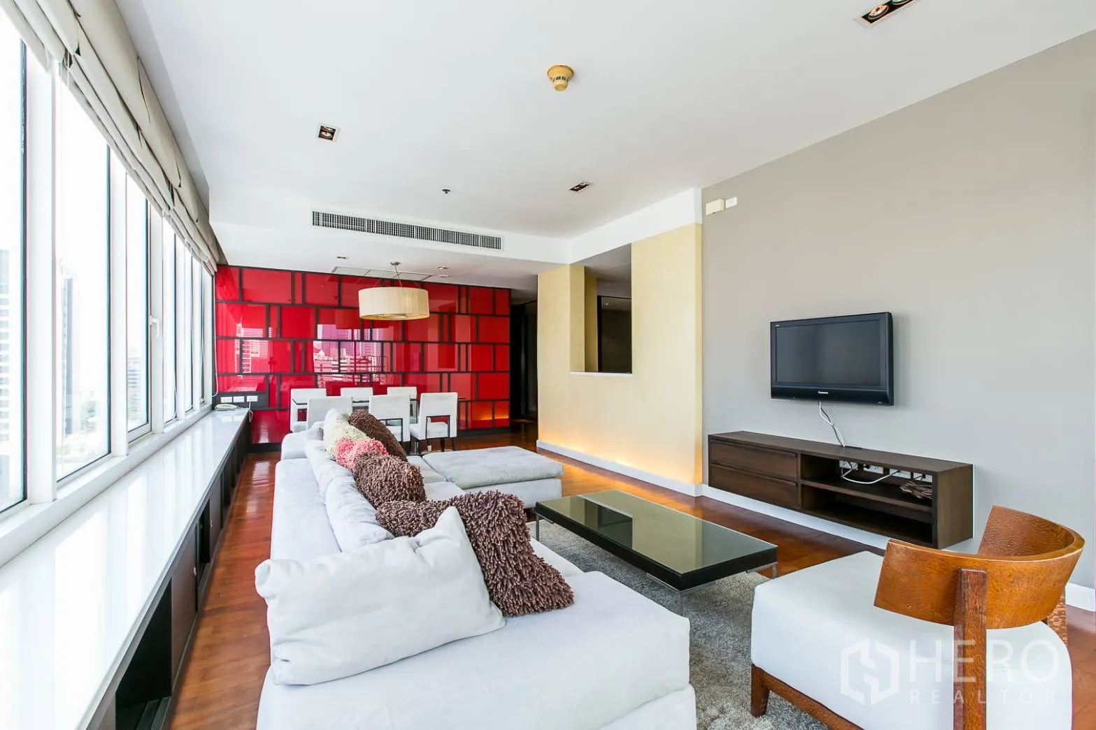 Condominium for rent or sale in Khlong Toei, Bangkok - Open-plan living and dining with sectional sofa, wall-mounted TV and red feature wall.