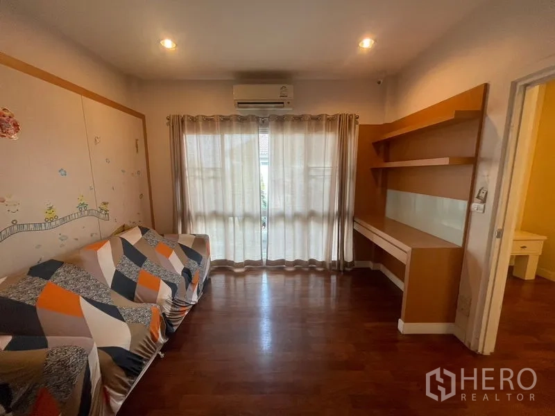 Detached House for rent or sale in Khan Na Yao, Bangkok - Cozy multipurpose room with built-in desk and shelves, plus balcony doors and wood flooring.